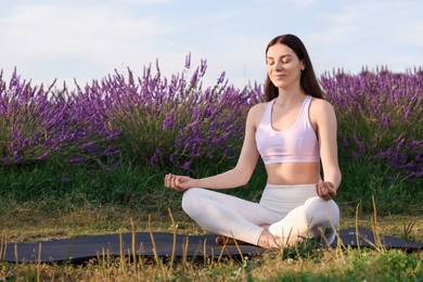 Photo of Beautiful woman practicing yoga near blooming lavender outdoors. Space for text