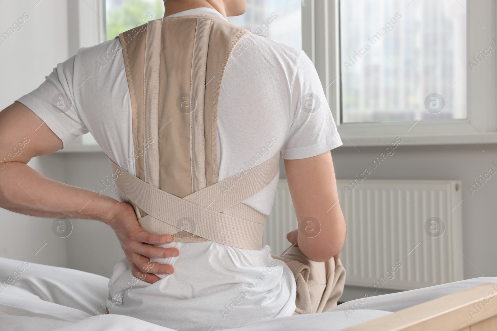 Photo of Closeup of man with orthopedic corset sitting in room, back view