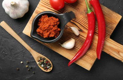 Photo of Dish with red curry paste and ingredients on black table, flat lay