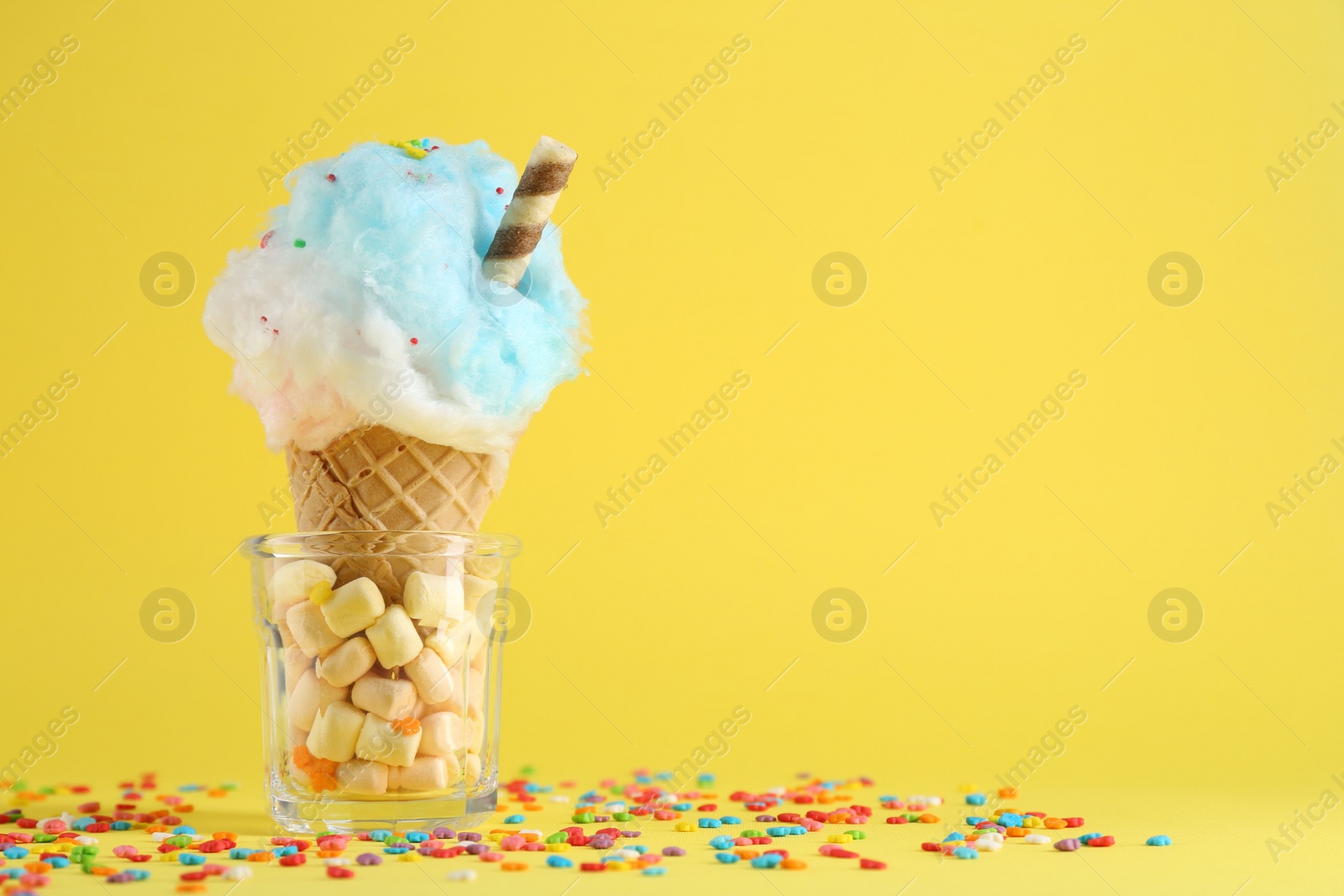 Photo of Sweet cotton candy in waffle cone on yellow background. Space for text