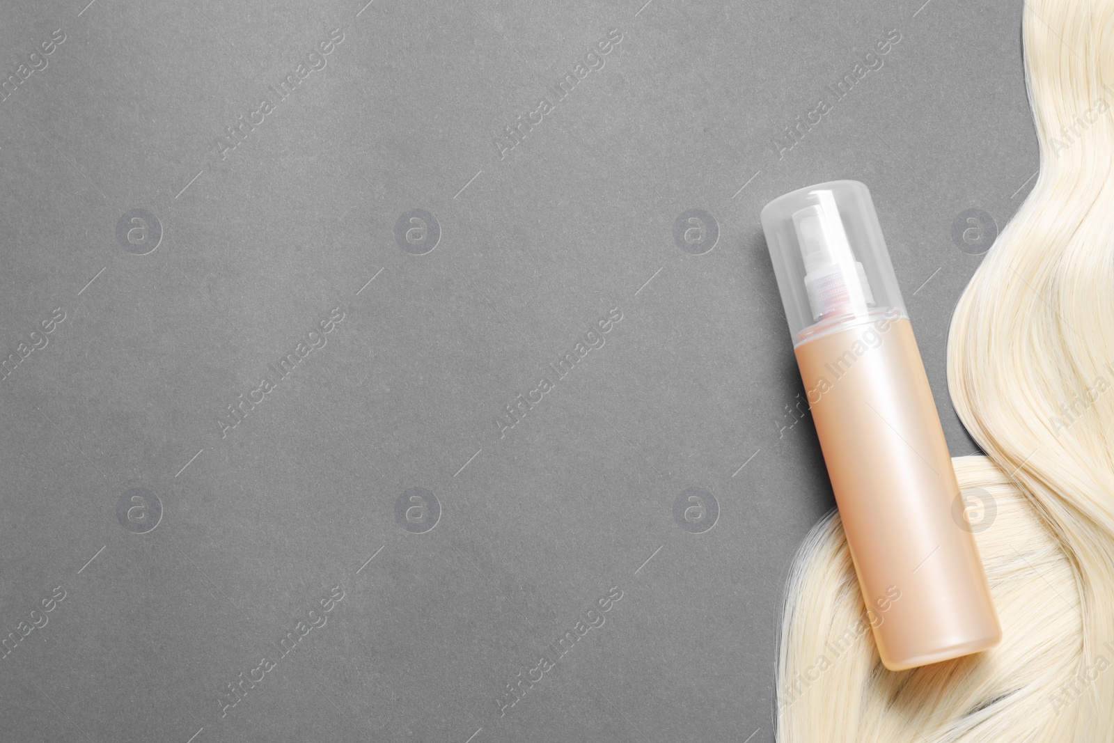 Photo of Spray bottle with thermal protection and lock of blonde hair on grey background, flat lay. Space for text