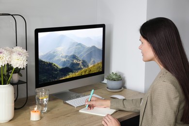 Photo of Young woman working at wooden table near computer in room