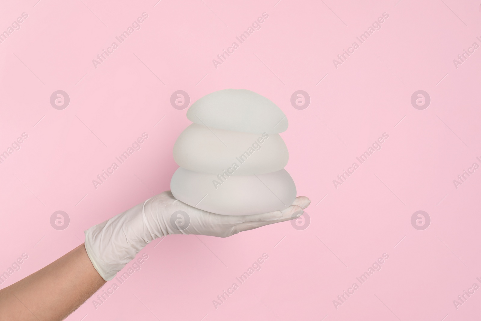 Photo of Doctor holding silicone implants for breast augmentation on color background, space for text. Cosmetic surgery