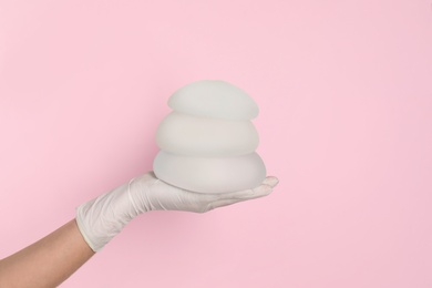 Photo of Doctor holding silicone implants for breast augmentation on color background, space for text. Cosmetic surgery