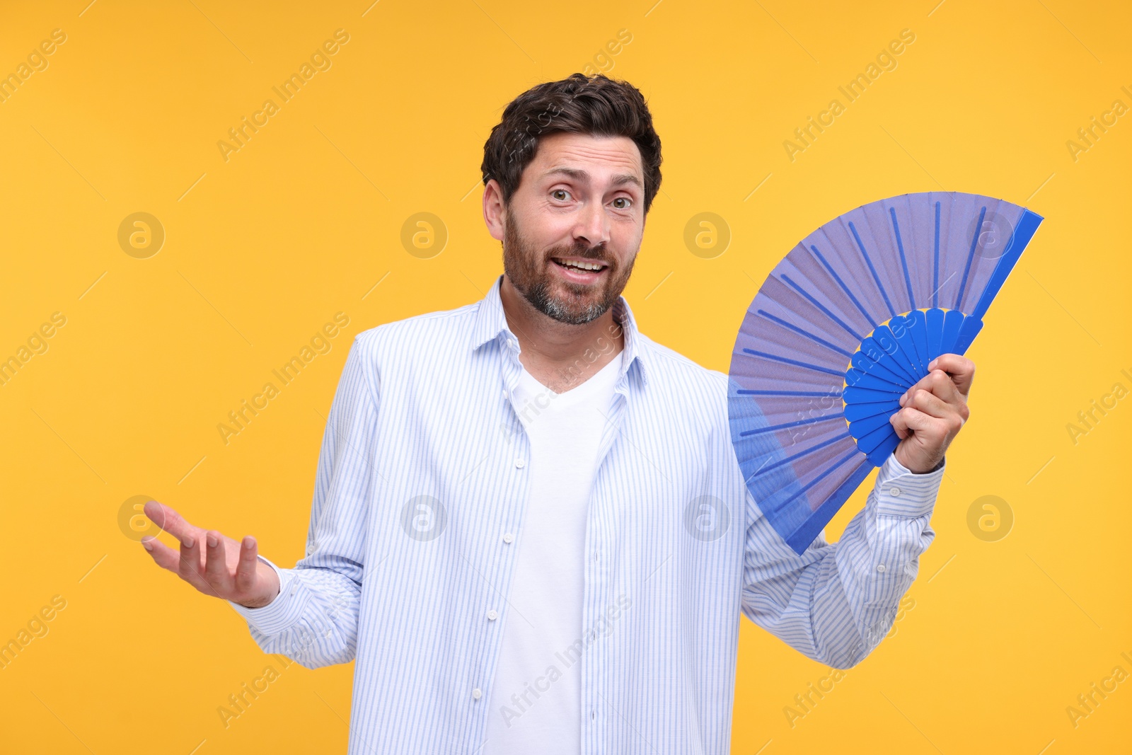 Photo of Confused man holding hand fan on orange background