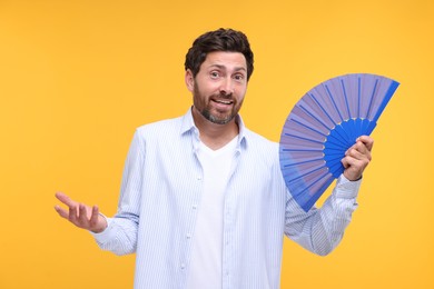 Confused man holding hand fan on orange background