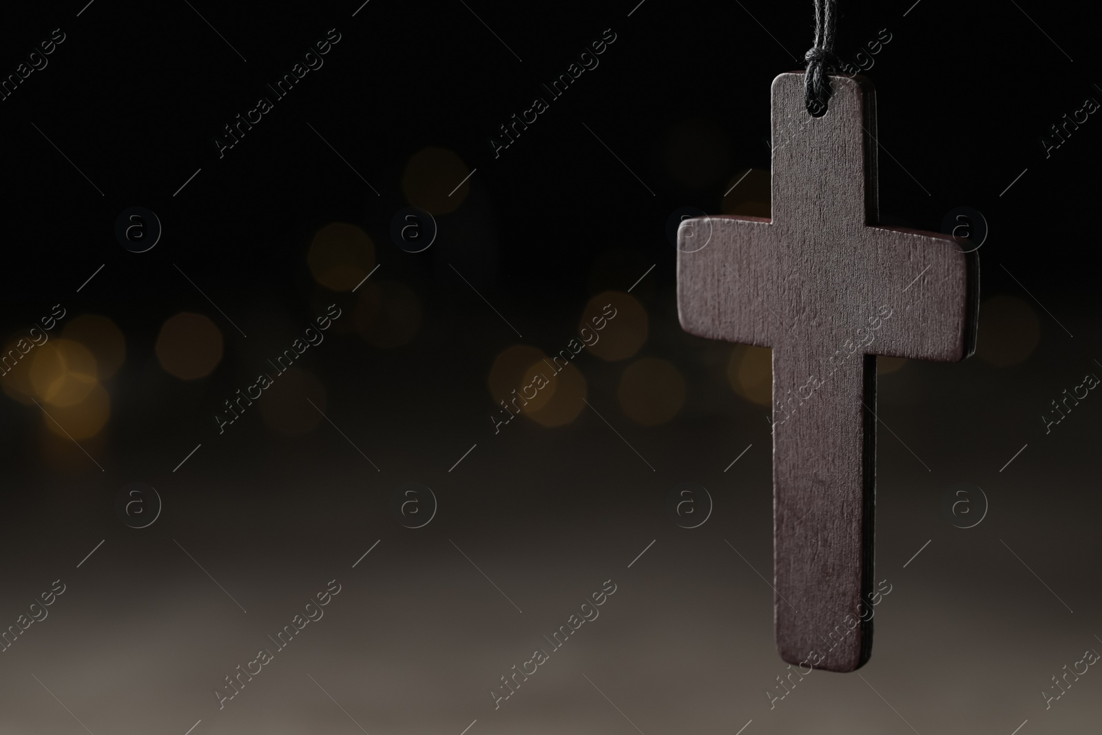 Photo of Wooden Christian cross against blurred lights, closeup. Space for text