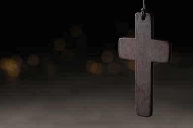 Photo of Wooden Christian cross against blurred lights, closeup. Space for text