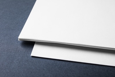 Blank paper sheets on dark grey background, closeup. Mock up for design