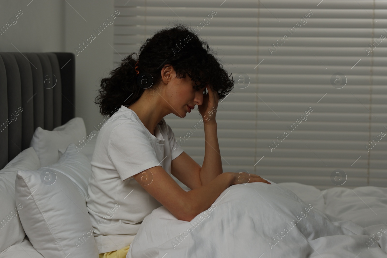 Photo of Young woman suffering from headache in bed at night