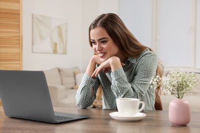 Happy woman with laptop at wooden table in room