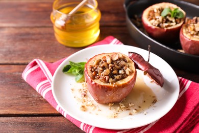 Photo of Tasty baked apples with nuts, honey and mint in dishware on wooden table, closeup