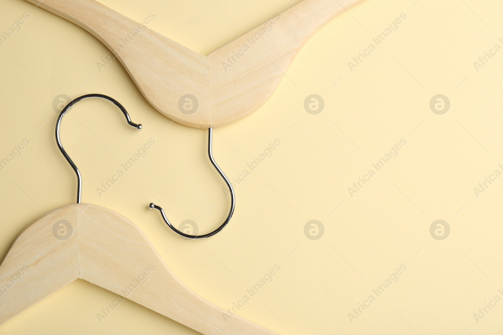 Photo of Wooden hangers on pale yellow background, flat lay. Space for text