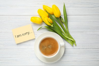 Apology. Yellow card with phrase I Am Sorry, cup of coffee and beautiful yellow tulips on white wooden table, flat lay