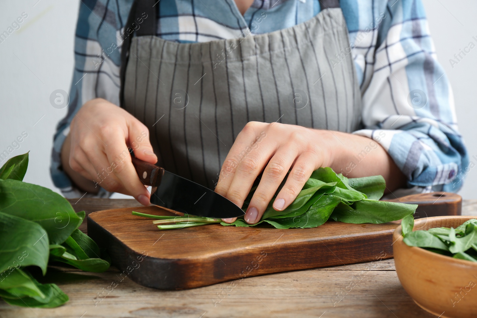 Photo of Woman cutting sorrel leaves at wooden table, closeup