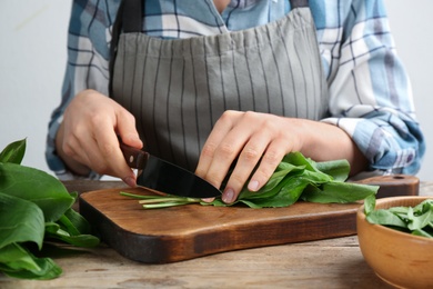Woman cutting sorrel leaves at wooden table, closeup