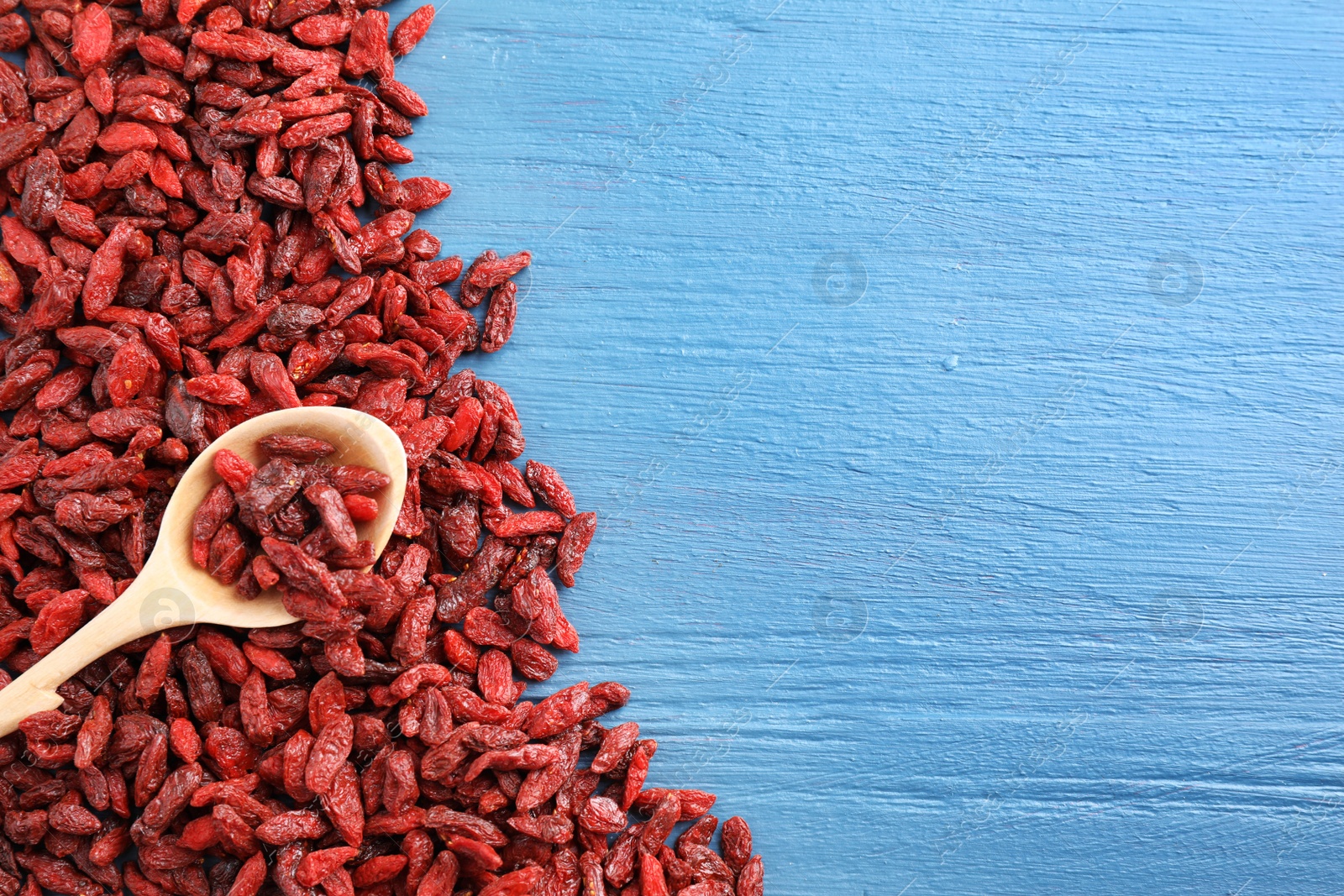 Photo of Dried goji berries on blue wooden table, top view. Space for text