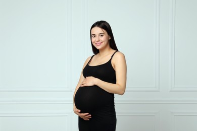 Photo of Beautiful pregnant woman in black dress near light grey wall