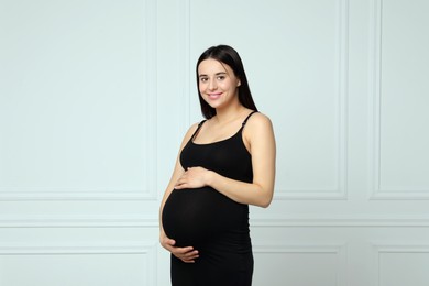 Beautiful pregnant woman in black dress near light grey wall