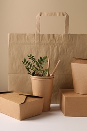 Eco friendly food packaging. Paper containers, bag, straws and green twigs on white table against beige background