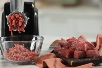 Electric meat grinder with beef mince on white table against blurred background, closeup