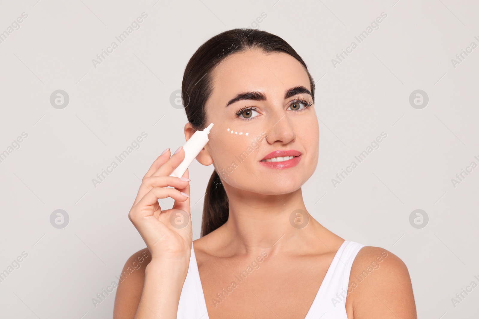 Photo of Woman with cosmetic product around eye on light background. Skin care