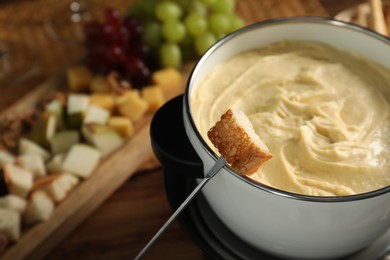 Fondue with tasty melted cheese, fork and piece of bread on wooden table, closeup