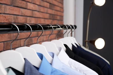 Wardrobe rack with stylish clothes near brick wall, closeup