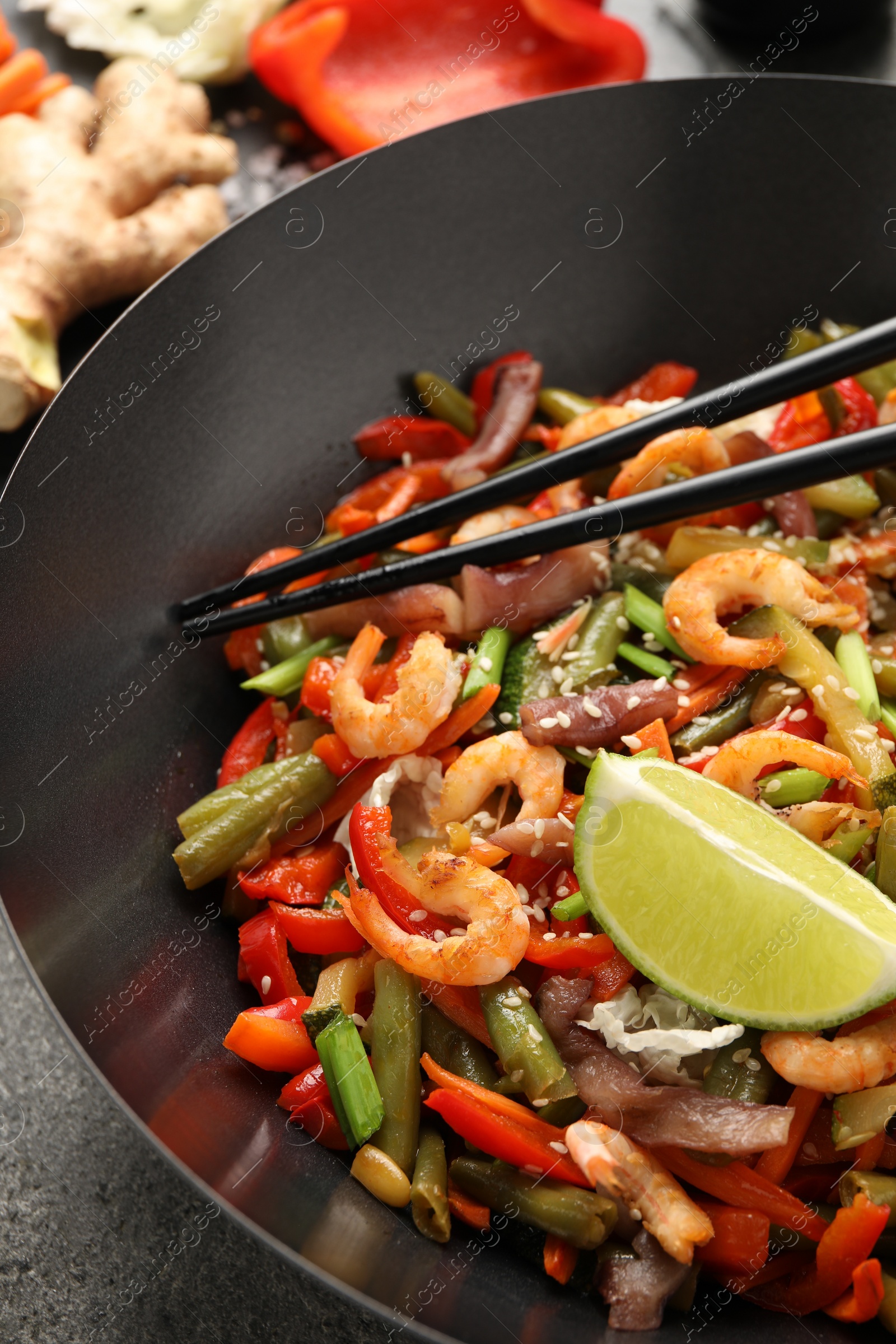 Photo of Shrimp stir fry with vegetables and chopsticks in wok on grey table, closeup