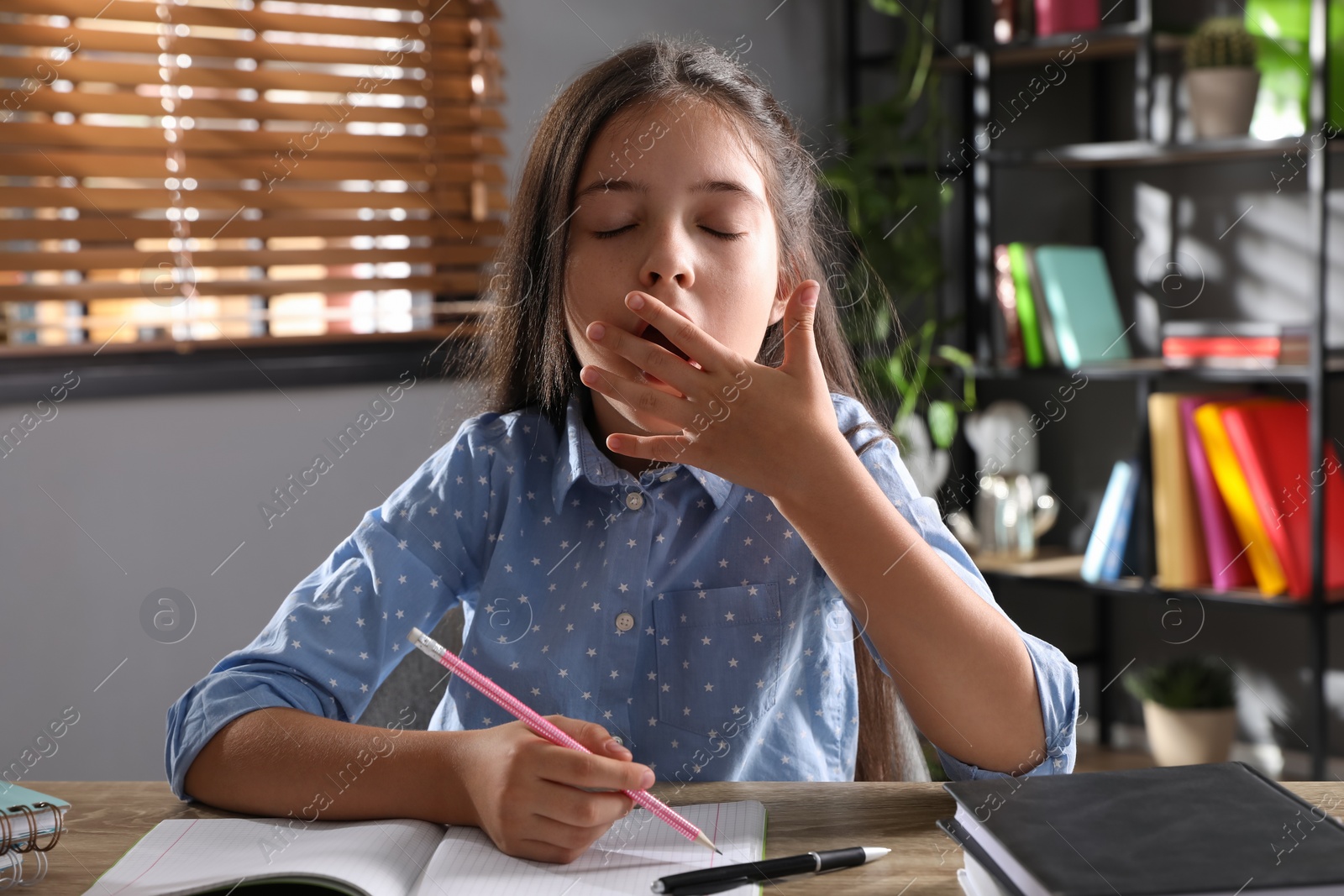 Photo of Tired preteen girl at table. Doing homework