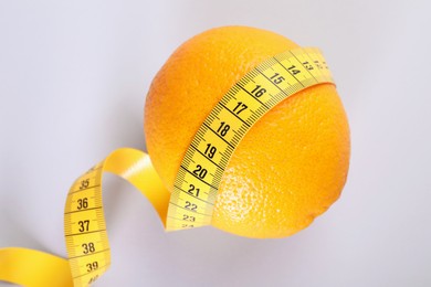 Photo of Cellulite problem. Orange with measuring tape on light grey background, top view