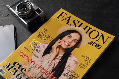 Photo of Fashion magazine and camera on black table, closeup