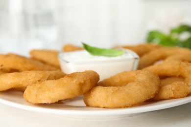 Photo of Delicious onion rings with sauce on white wooden table, closeup
