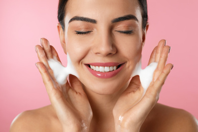 Young woman applying cosmetic product on pink background, closeup. Washing routine