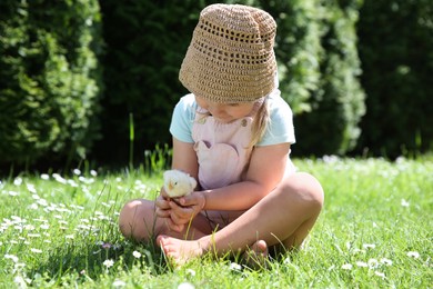 Photo of Cute little girl with chick on green grass outdoors. Baby animal