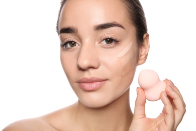 Young woman applying foundation on her face against white background