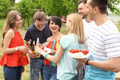 Photo of Young people with bottles of beer and food outdoors. Summer barbecue