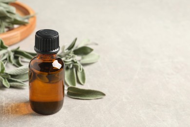 Photo of Bottle of essential sage oil and leaves on light grey table. Space for text