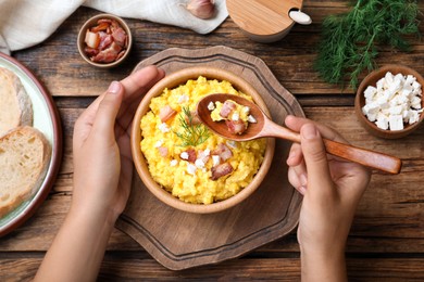 Woman eating banosh with brynza and pork cracklings at wooden table, top view. Traditional Ukrainian dish