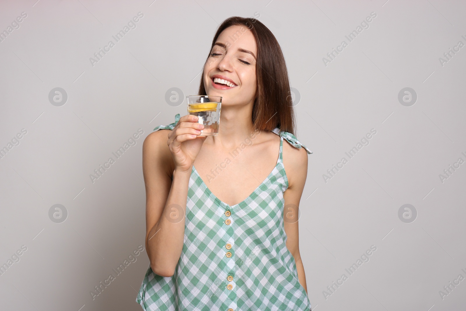 Photo of Young woman drinking lemon water on light background