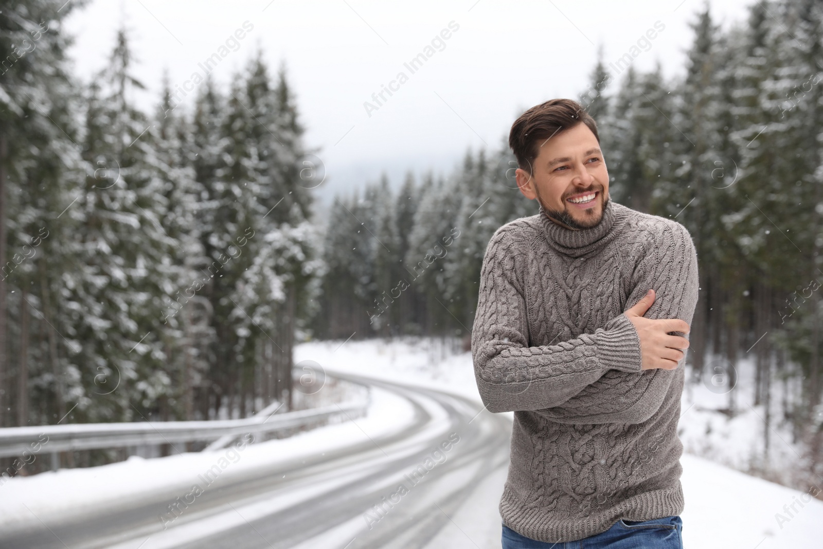 Photo of Man in warm sweater near snowy forest, space for text. Winter vacation