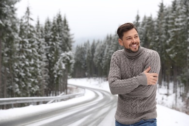 Photo of Man in warm sweater near snowy forest, space for text. Winter vacation