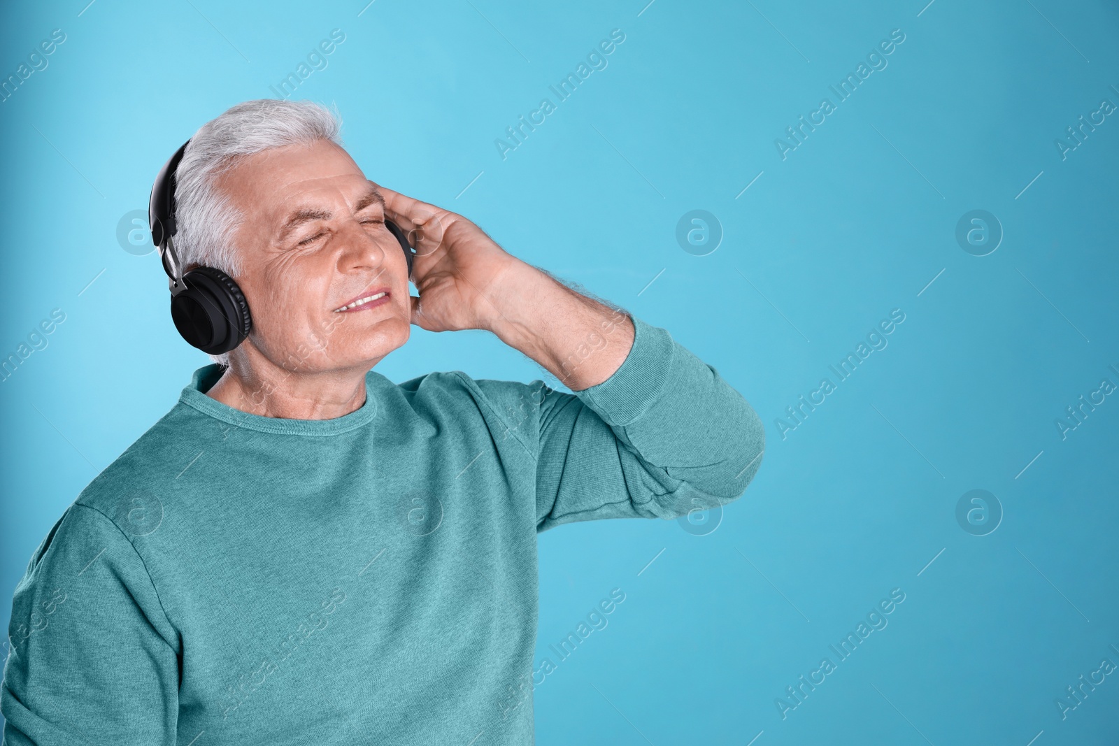 Photo of Mature man enjoying music in headphones on color background. Space for text