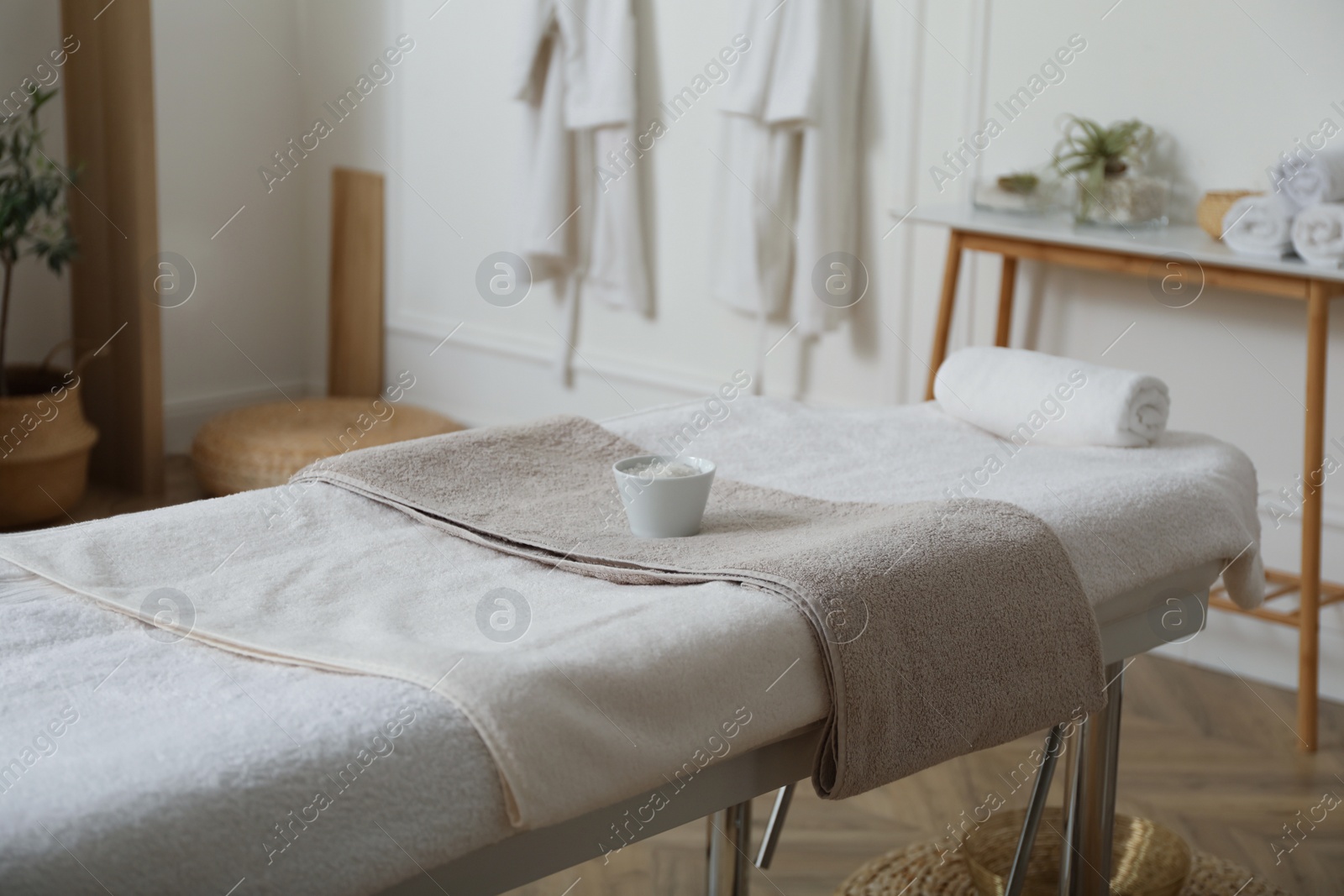 Photo of Sea salt for spa procedure and soft terry towels on massage table in salon