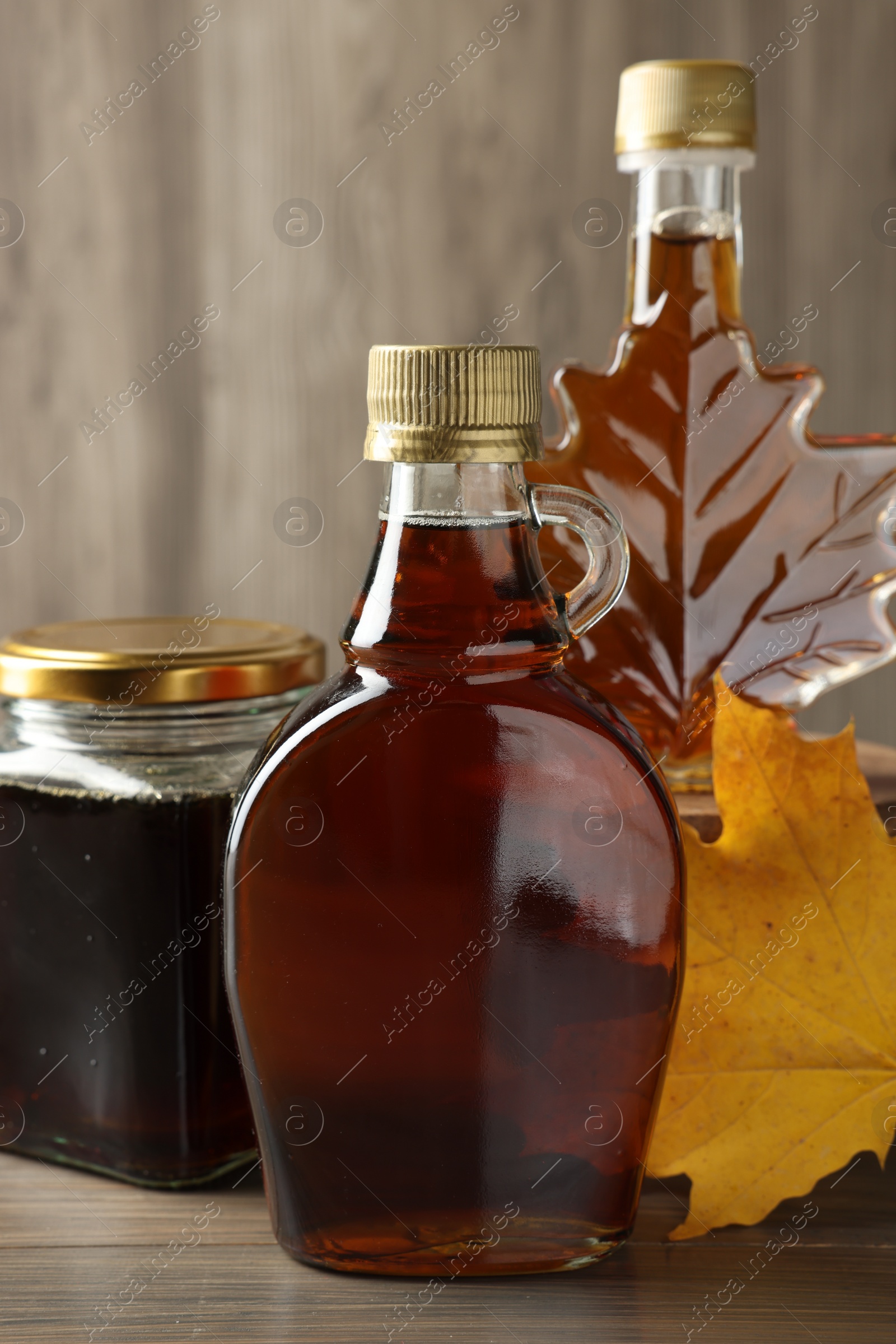 Photo of Bottles and jar of tasty maple syrup on wooden table