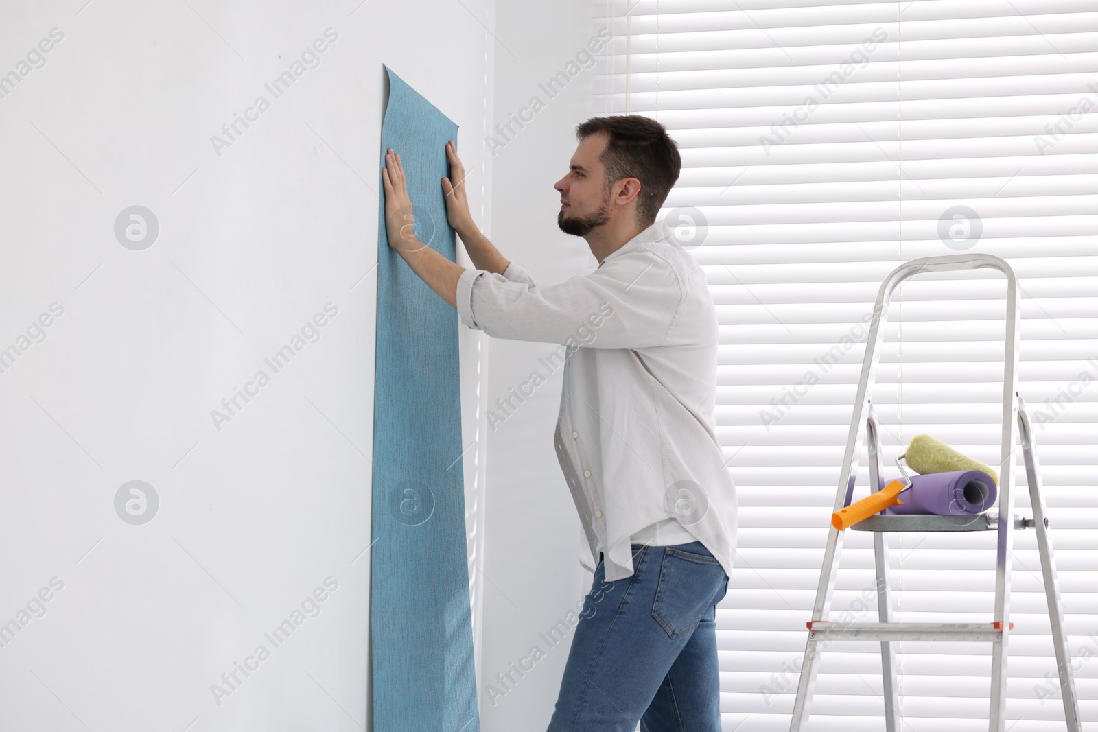 Photo of Man hanging light blue wallpaper in room