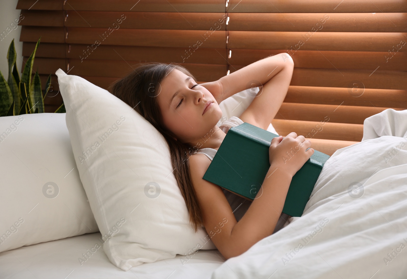 Photo of Cute preteen girl with book sleeping in bed near window