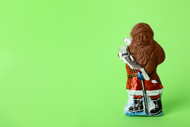 Photo of Sweet chocolate Santa Claus candy in slightly open foil wrapper on light green background, space for text