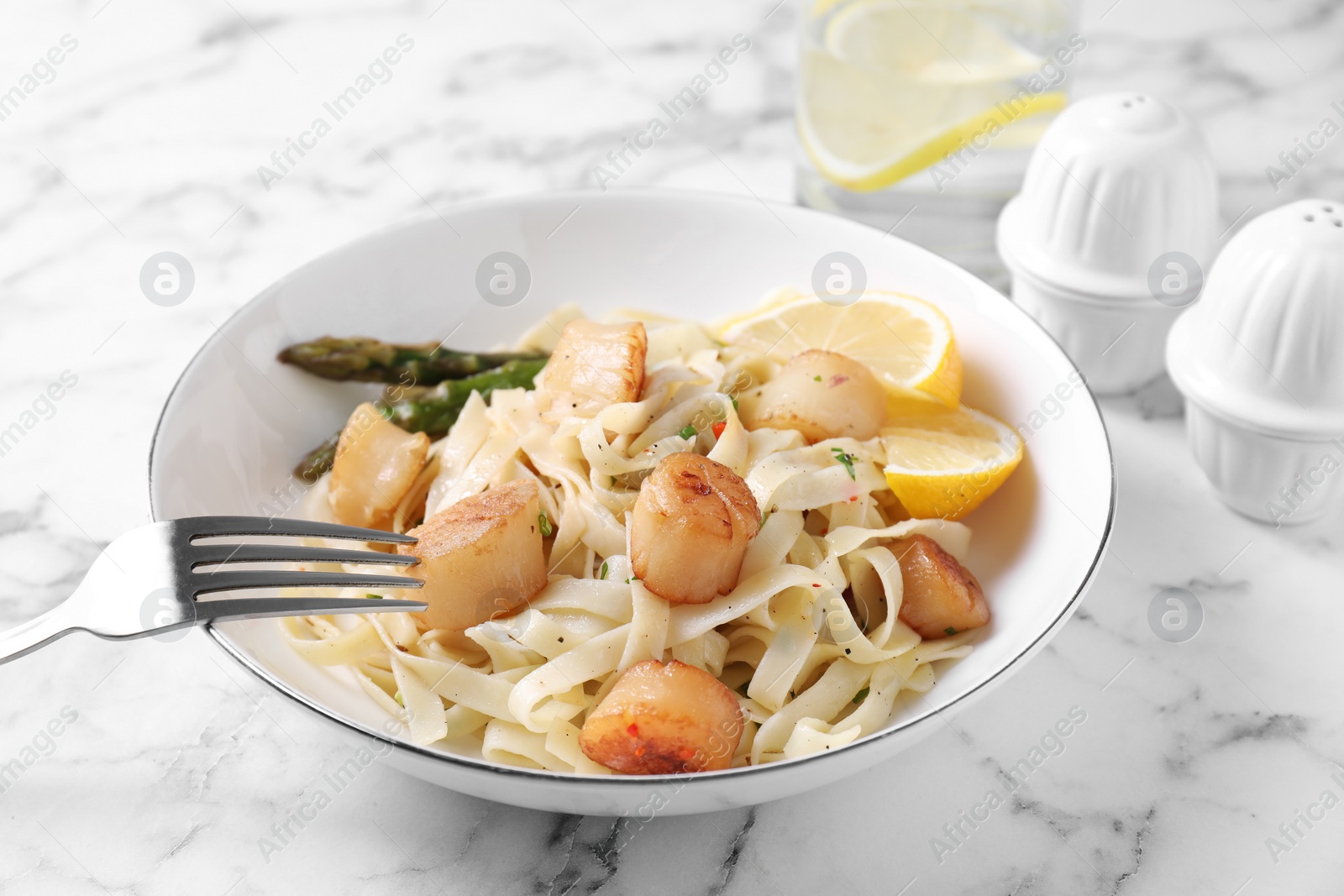 Photo of Delicious scallop pasta with asparagus and lemon on white marble table