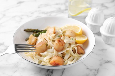 Photo of Delicious scallop pasta with asparagus and lemon on white marble table